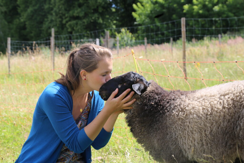 Denise vom deutschen Tierschutzbüro küsst ein Schaf auf den Kopf. Sie befinden sich auf einer grünen Weide.
